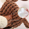 A hand is holding a brown plush squeaky donkey dog toy with a white nose, showing its textured surface.