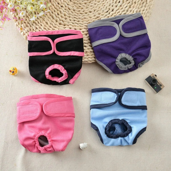 A collection of reusable dog diapers in pink, purple, and blue colors shown on a light fabric background.