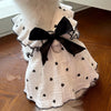 A white lightweight cotton dog dress with a black heart print and a large black bow, displayed on a wooden surface.