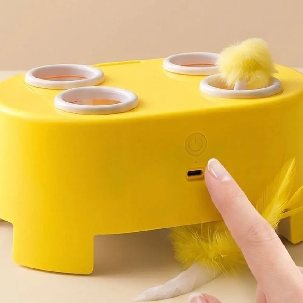 A yellow interactive whack-a-mole cat toy with a rotating base and yellow feathers is being operated by a finger.