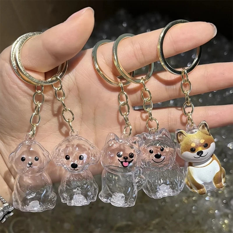 Eine Hand hält eine Reihe klarer Glaspuppy-Anhänger, die an goldfarbenen Metall-Schlüsschen hängt.