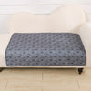 A gray pet pee pad is placed on a cream-colored upholstered surface.