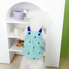 A white fluffy dog dressed in a green polka-dot dress with blue trim, standing in a white shelf display.