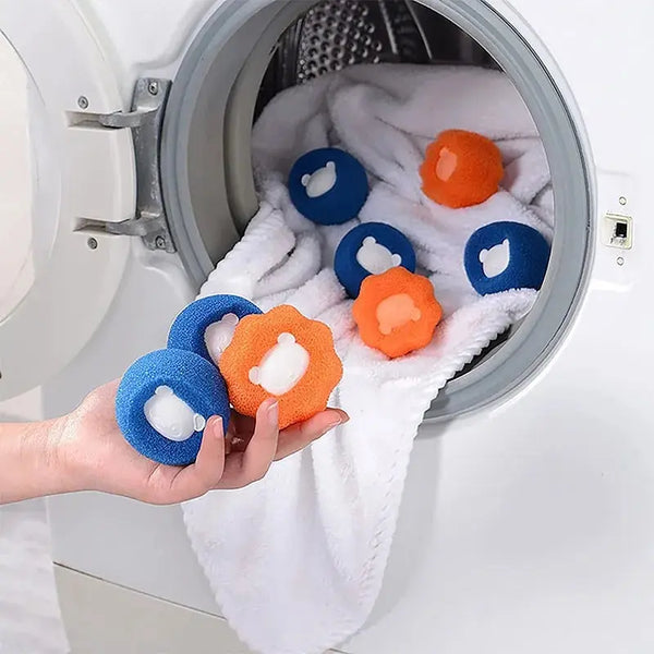 A hand is holding several reusable pet hair and lint removal balls in blue and orange colors inside a washing machine drum.