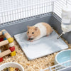 Ein kleiner brauner Hamster ruht auf einer quadratischen weißen Kühlmatte in einem Drahtkäfig.