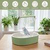 A green automatic bird shower bath for parrots sitting on a wooden table with potted plants in the background.