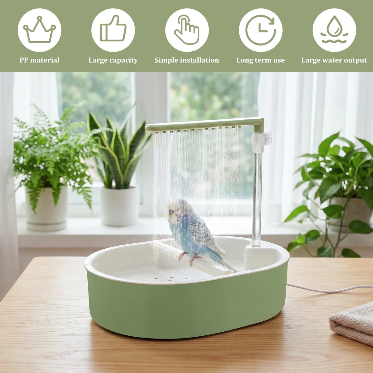 A green automatic bird shower bath for parrots sitting on a wooden table with potted plants in the background.