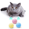 A gray cat is sitting next to a set of colorful, spherical toys with sound emitting waves.