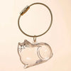 A clear glass charm shaped like a cat is suspended from a braided gold-colored cord.