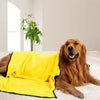 Un golden retriever est allongé sur une surface blanche à côté d'une serviette de bain ultra-absorbante jaune vif.
