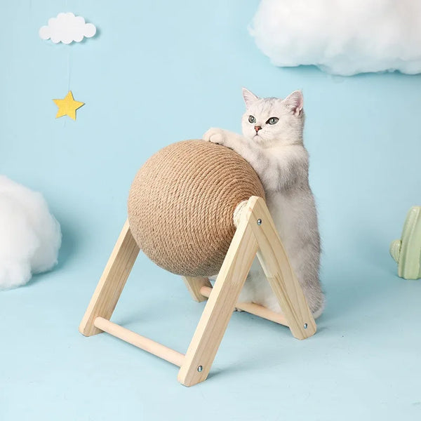 A fluffy gray cat sits next to a large, round sisal rope ball toy supported by a wooden A-frame base.
