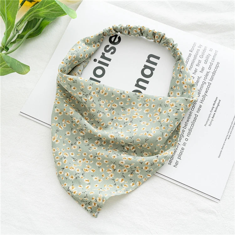 A light green bohemian paisley triangle head scarf draped on a white surface next to a magazine.