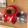 A brown capybara plush doll wearing a red hoodie with white trim, hanging by a gold chain.
