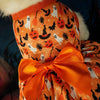 Vestido de cosplay para perro naranja con estampado de calabazas y murciélagos y un lazo naranja brillante.