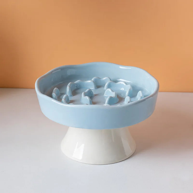Un bol en céramique bleu clair à alimentation lente pour animaux, posé sur un piédestal blanc sur fond orange.