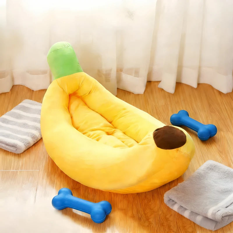 A yellow banana-shaped plush pet bed for cats and dogs resting on a wooden floor with gray towels nearby.
