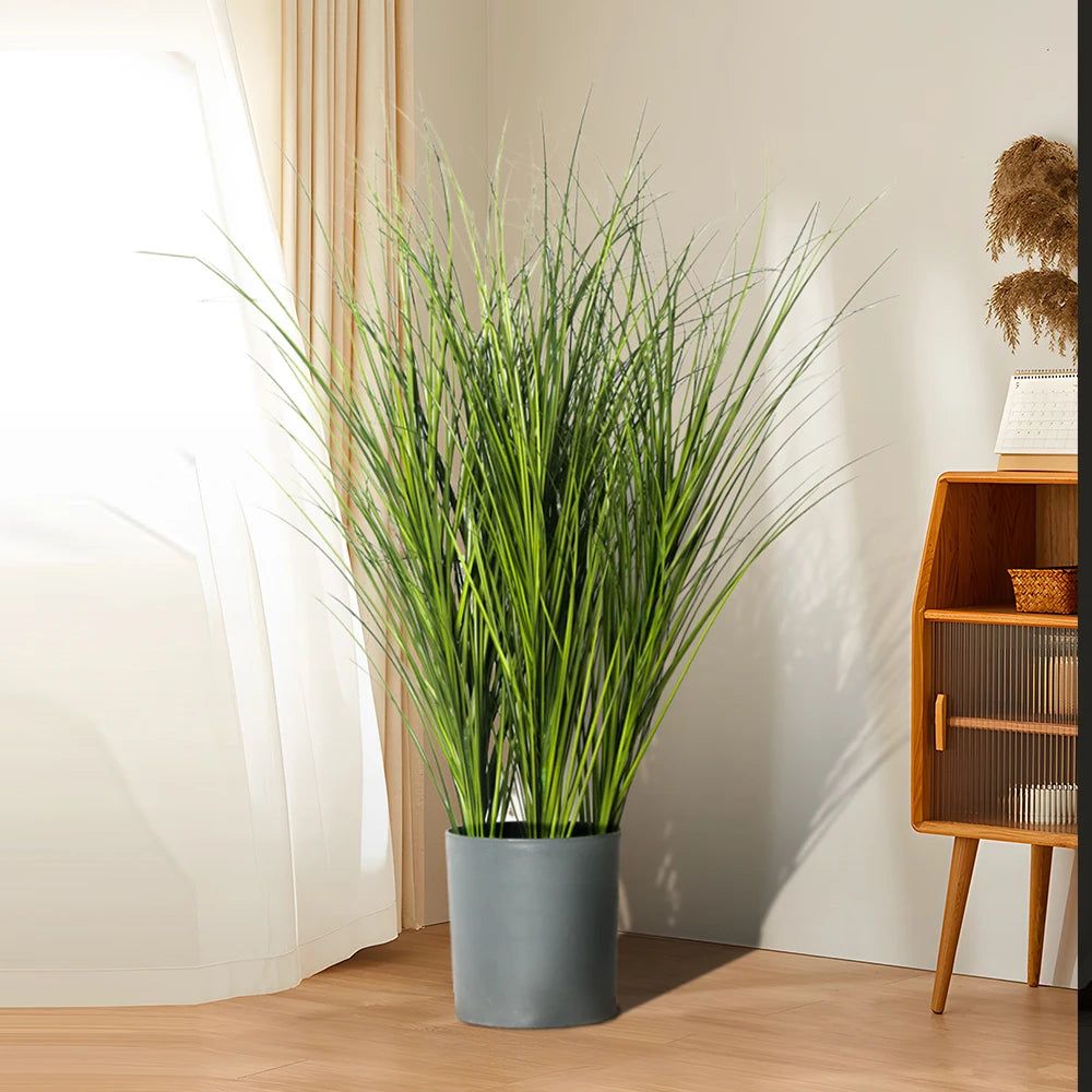 A tall potted artificial reed grass bouquet in a gray planter placed next to a wooden shelf.