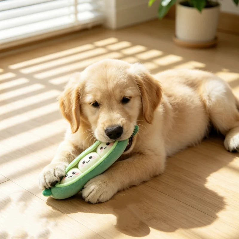 A light golden puppy lies on a wooden floor chewing a green plush sausage dog chew toy.