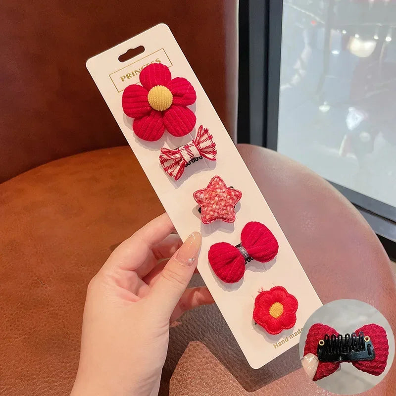 A hand holds a white card displaying five red flower-shaped baby hair clips with white and yellow accents.