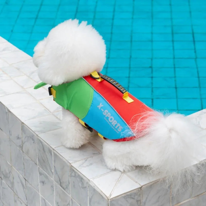A white, fluffy dog life jacket with green and red accents rests on a white tiled ledge next to blue water.