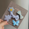 Una mano sostiene un paquete de cinco lazos de tela hechos a mano con flores y mariposas para clips de pelo de mascotas.