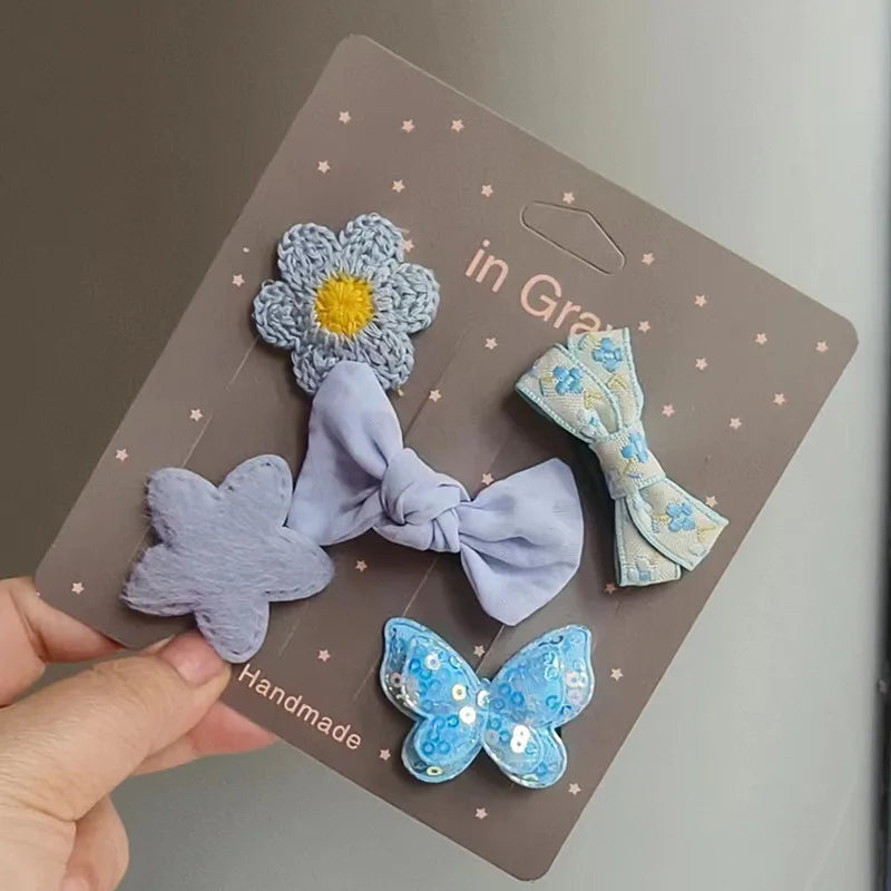 Una mano sostiene un paquete de cinco lazos de tela hechos a mano con flores y mariposas para clips de pelo de mascotas.