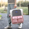 A person is holding a pink and white ventilated cat carrier backpack with adjustable straps outdoors.