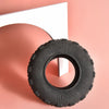 A black rubber chew toy tire resting on a pink surface next to a white object.
