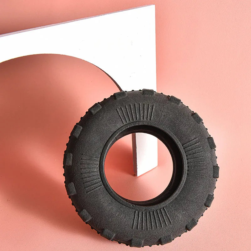 A black rubber chew toy tire resting on a pink surface next to a white object.