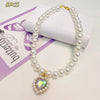 A necklace featuring white pearls with a heart-shaped pendant, displayed on a purple background.