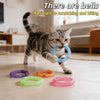A tabby cat is playing with various colored donut-shaped chew toys, including a blue one with a bell.