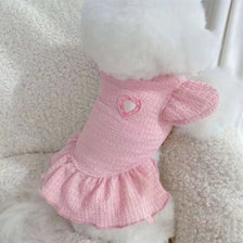 A pink knitted dog dress for a pet with a heart detail and ruffled hem.