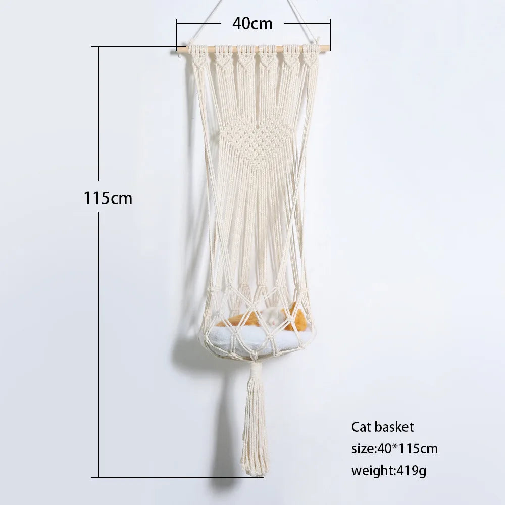 A beige macrame cat basket hammock hanging against a white wall.