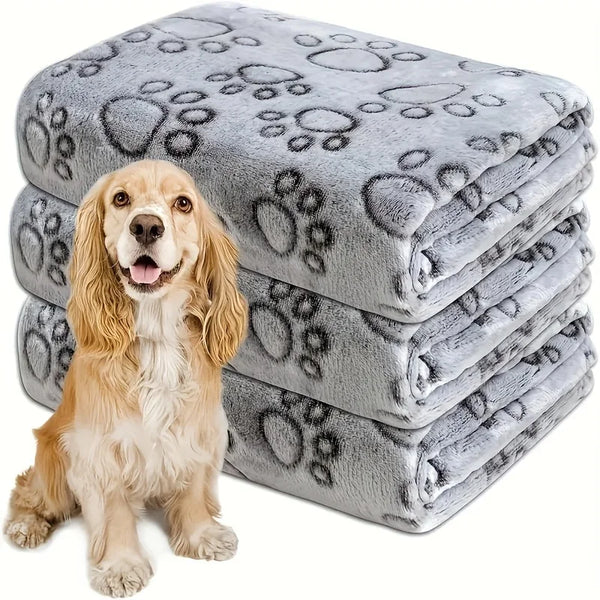 A stack of grey flannel pet blankets featuring a paw print design, with a golden retriever dog sitting in front.