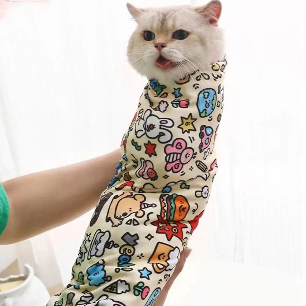 A fluffy ginger cat wearing a colorful self-adhesive pet swaddle for nail clipping and restraint.
