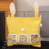 Un sac à foin jaune en toile avec trois compartiments pour petits mangeoires d'animaux de compagnie, exposé sur une surface s