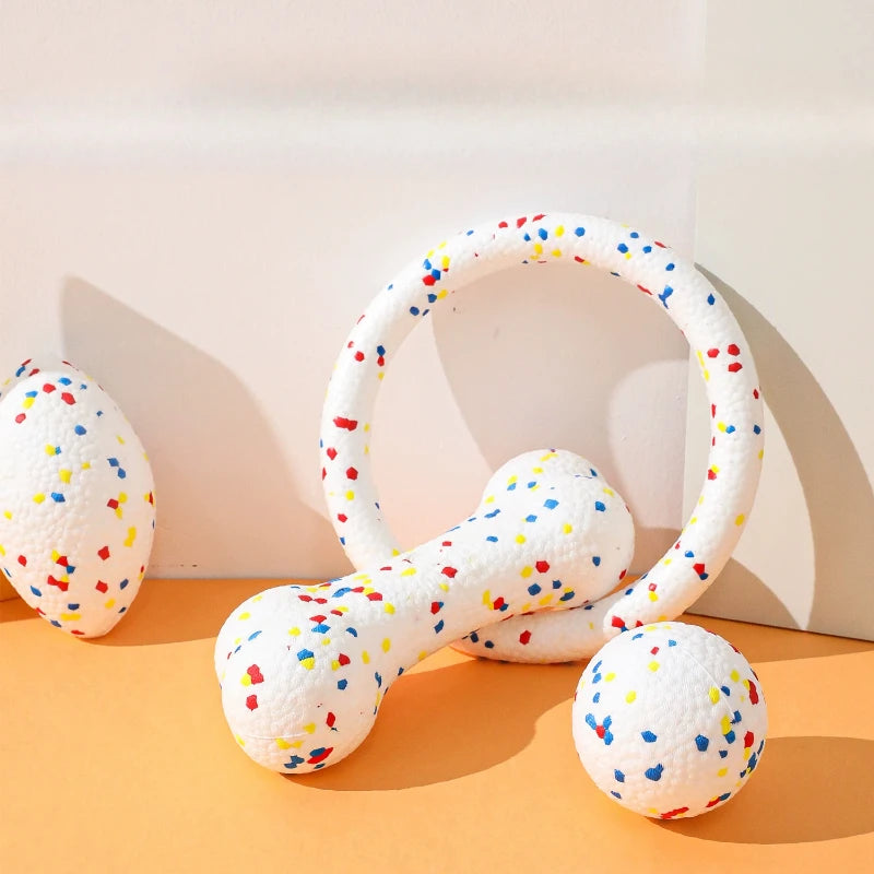 A white, textured chew ball and a bone-shaped chew toy for dogs are displayed on an orange surface.