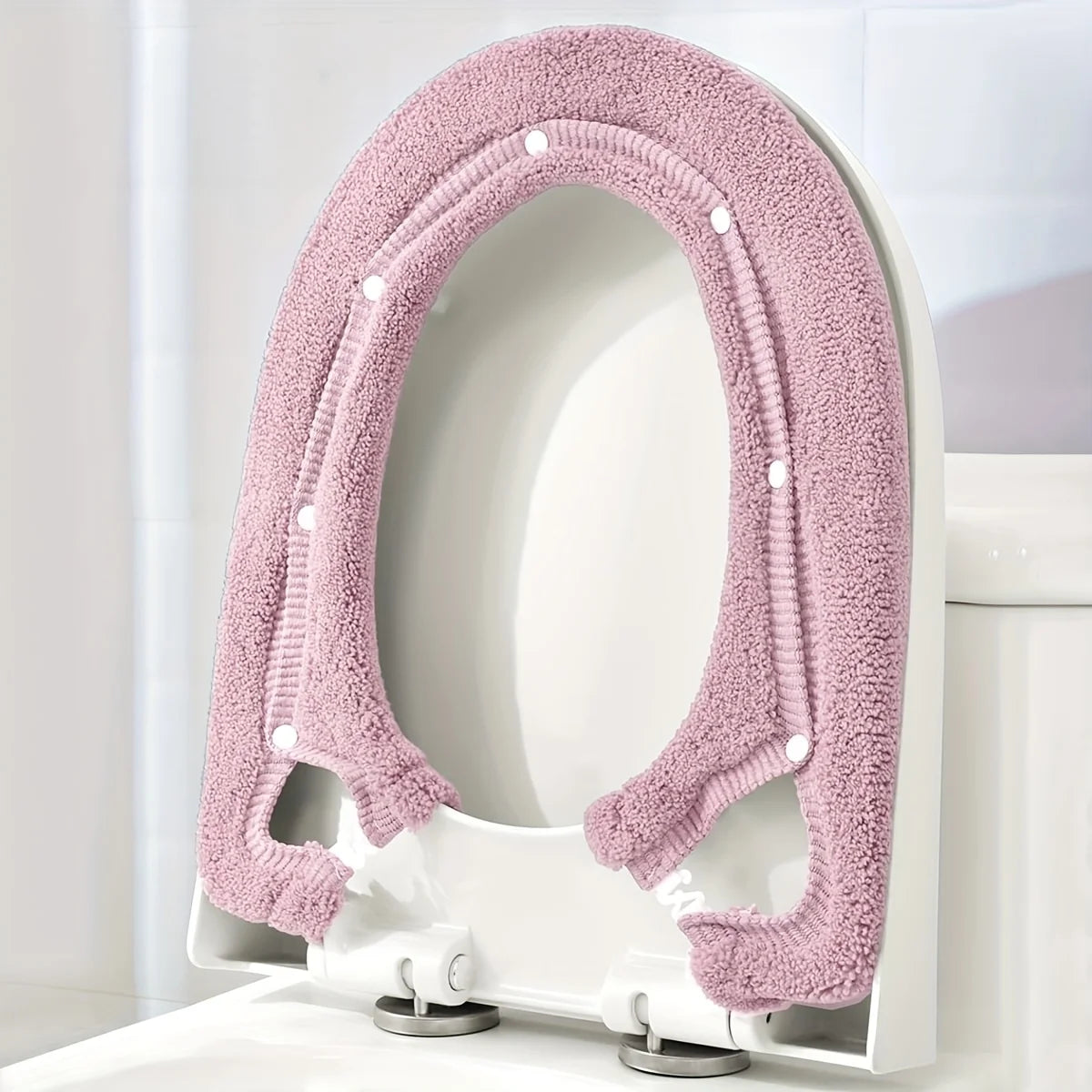 A pink plush non-slip toilet seat cover is shown installed on a white toilet bowl.