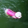 A white dog wearing a pink summer life vest swimming in green water.