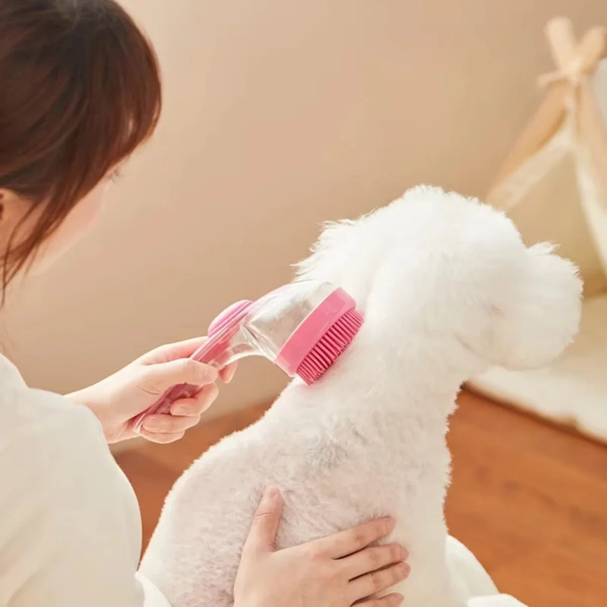 A person is using a pink silicone pet bathing brush on a white dog.
