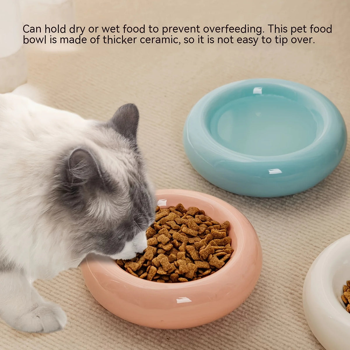 A cat is eating dry food from a pink ceramic pet bowl on a beige surface.