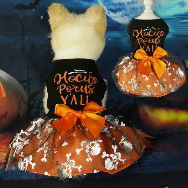 A fluffy white dog wearing a black dress with gold embroidery and an orange bow, displayed against a dark blue background.