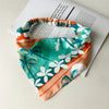 Un primer plano de una diadema elástica con estampado floral boho en tonos verde azulado, naranja y blanco.