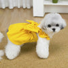 A white dog wearing a yellow vintage corduroy pet dress with a bow and ruffle skirt.