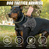 A black dog wearing a tactical harness with a reflective vest, being held by a person in camouflage clothing.