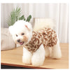 A fluffy white dog wearing a leopard print princess dress sitting on a wooden surface.