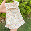 A light floral summer dress for dogs or cats with ruffled edges being held up against a green outdoor background.