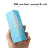 A hand holds a light blue silicone hair removal brush with white bristles.