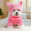 A white dog wearing a pink flannel hoodie with red stripes, sitting on a white bed.