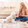 A young woman is sitting on the floor with a white dog, next to pink pads labeled Keep Clean and Reduce Odor.